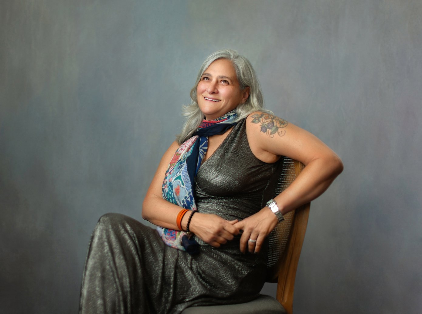 Grey photo backdrop with a photo of Professor Dillard, silver shoulder length hair white woman, sitting in a chair.