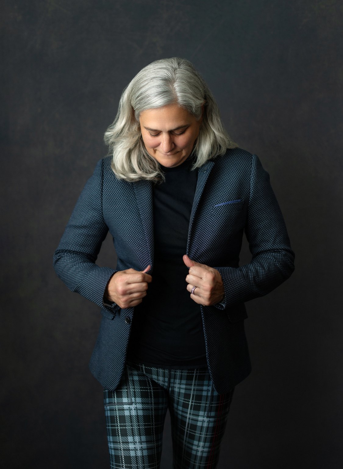 a person with silver hair wearing a jacket and plaid pants against a dark grey photo backdrop. On top of the photo is text in all caps that says "Law Professor."